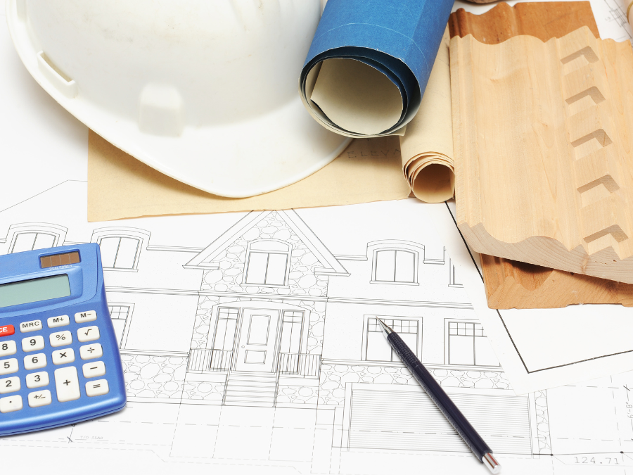 Kalkulator, projekt domu, próbki materiałów i kask na biurku, co odnosi się do precyzyjnego przygotowania kosztorysów budowlanych.